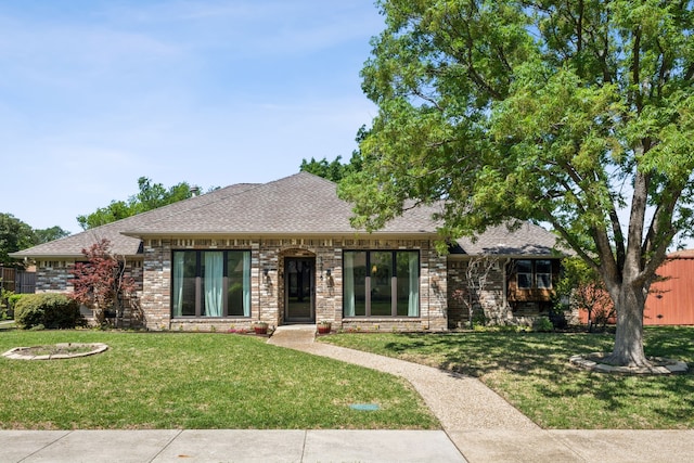 view of front facade with roof with shingles, brick siding, and a front yard
