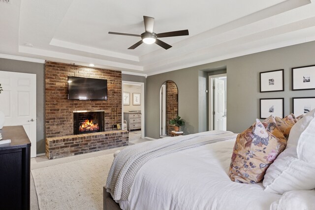 bedroom with a fireplace, carpet floors, arched walkways, a tray ceiling, and ornamental molding