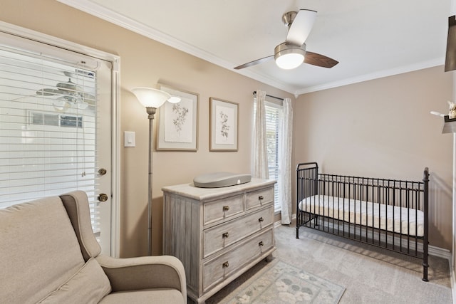 bedroom with crown molding, a nursery area, light colored carpet, a ceiling fan, and baseboards