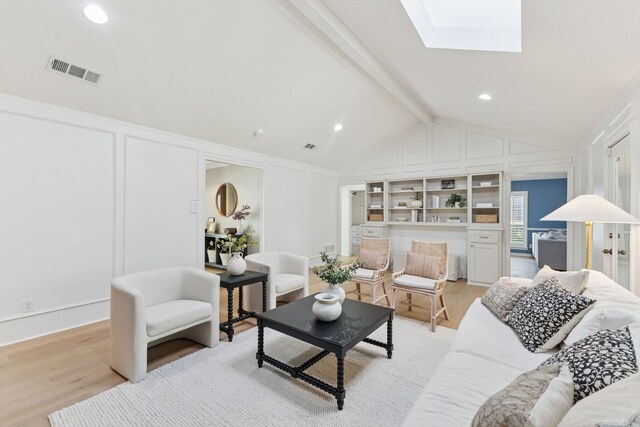 living area with a decorative wall, lofted ceiling with skylight, light wood-style flooring, and visible vents