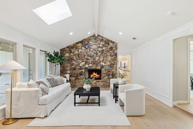 living area with a fireplace, visible vents, vaulted ceiling with skylight, and light wood-style floors