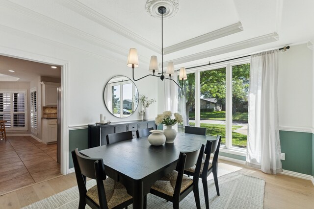 dining space with baseboards, ornamental molding, a tray ceiling, and light wood finished floors
