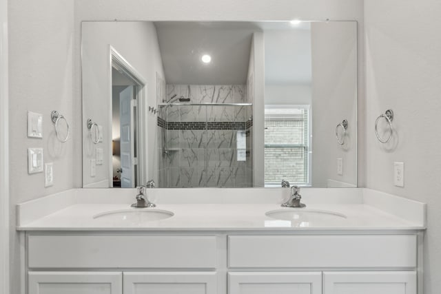 bathroom with double vanity, a sink, and tiled shower