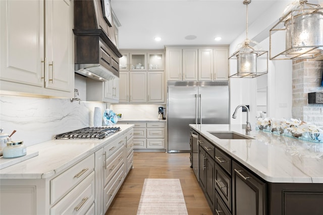 kitchen featuring hanging light fixtures, appliances with stainless steel finishes, a sink, light wood-style floors, and premium range hood