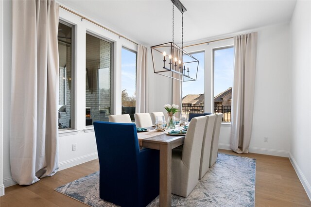 dining room with an inviting chandelier, baseboards, a warm lit fireplace, and light wood-style flooring