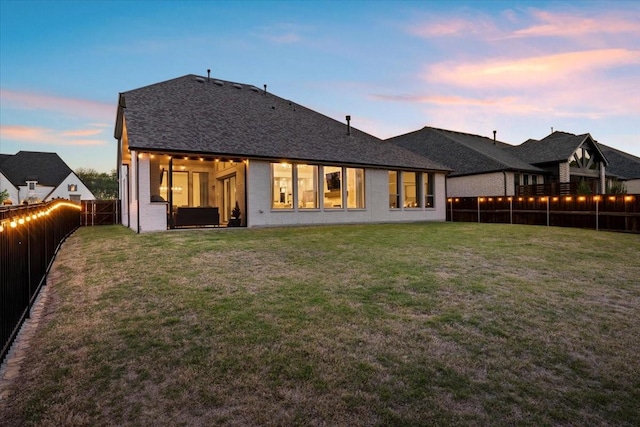 back of property at dusk with a fenced backyard, a yard, and brick siding