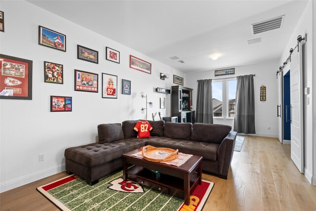 living area with visible vents, a barn door, baseboards, and light wood-type flooring