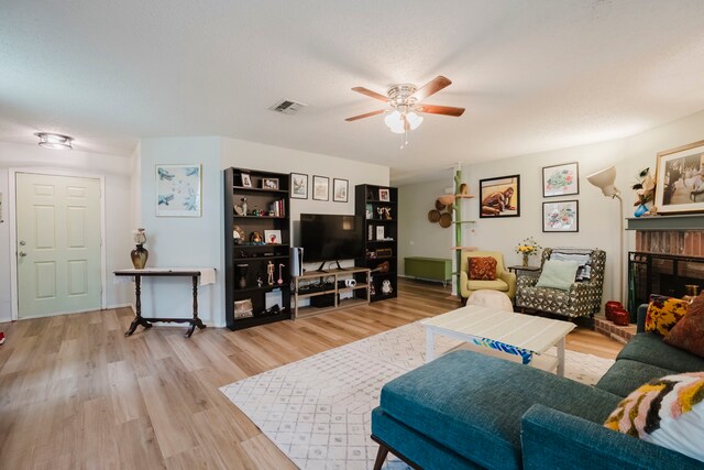 living area featuring a brick fireplace, a ceiling fan, wood finished floors, and visible vents
