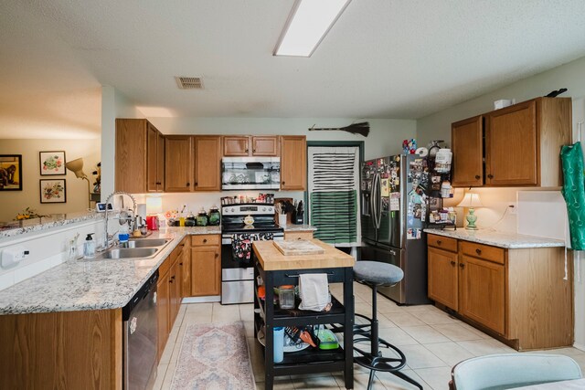 kitchen with a sink, appliances with stainless steel finishes, light tile patterned floors, and brown cabinets