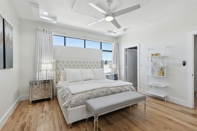bedroom featuring baseboards, a ceiling fan, light wood-style flooring, and a tray ceiling