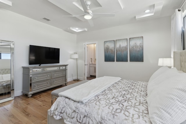 bedroom with ensuite bath, a ceiling fan, baseboards, wood finished floors, and visible vents
