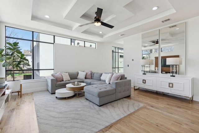 living area with ceiling fan, light wood-style flooring, and a raised ceiling