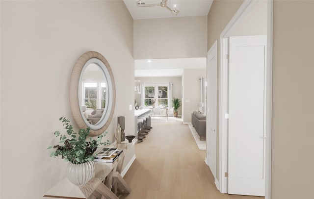 hallway with light wood-type flooring, baseboards, a towering ceiling, and an inviting chandelier
