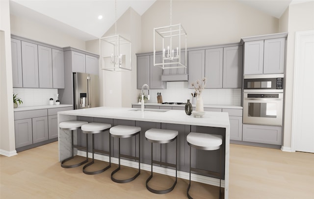 kitchen with gray cabinetry, stainless steel appliances, light wood finished floors, and a notable chandelier