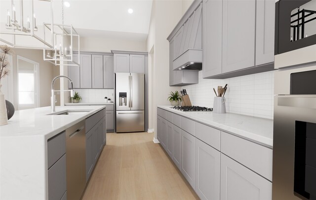 kitchen featuring appliances with stainless steel finishes, light wood-type flooring, a sink, gray cabinetry, and an inviting chandelier