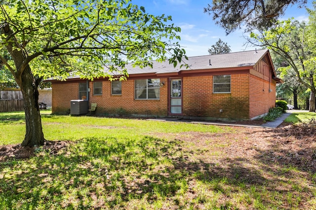 back of house featuring brick siding, central AC unit, fence, and a yard