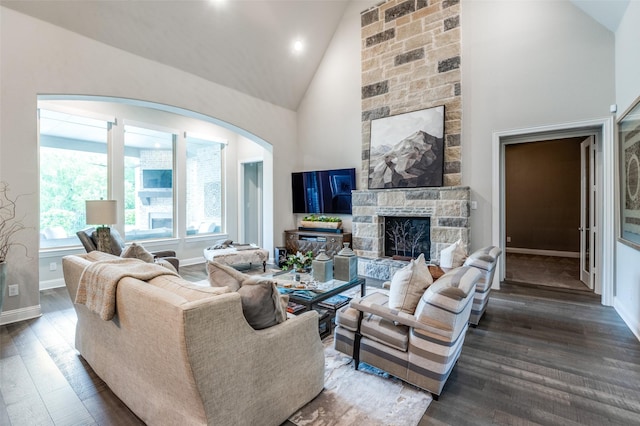 living room with arched walkways, high vaulted ceiling, a stone fireplace, baseboards, and wood finished floors