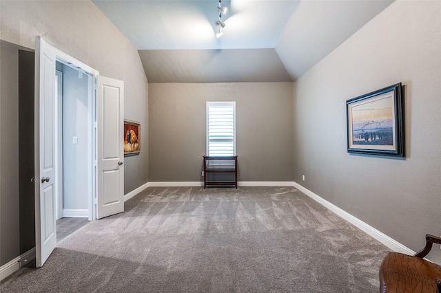 unfurnished bedroom featuring carpet floors, baseboards, rail lighting, and lofted ceiling