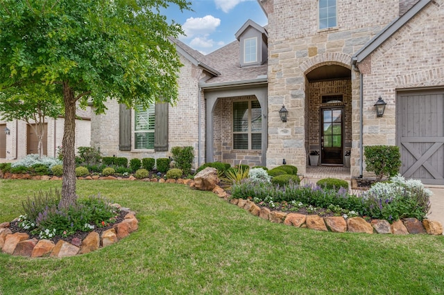 property entrance with a lawn, roof with shingles, stone siding, and brick siding