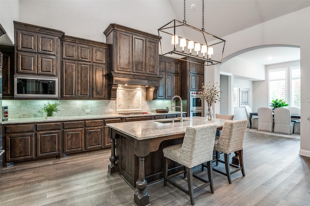 kitchen with a breakfast bar area, high vaulted ceiling, arched walkways, a sink, and stainless steel appliances