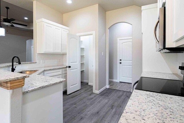 kitchen with white cabinets, ceiling fan, light stone countertops, a sink, and dark wood-style floors