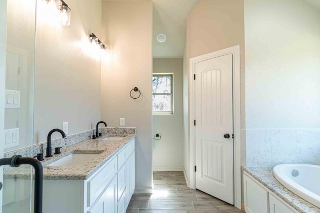 full bath featuring baseboards, a sink, a tub to relax in, and wood finished floors