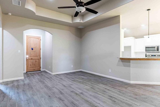 unfurnished living room with a raised ceiling, arched walkways, a ceiling fan, wood finished floors, and visible vents