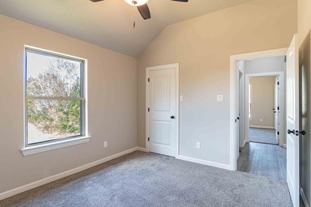 unfurnished bedroom featuring baseboards, carpet, lofted ceiling, and multiple windows