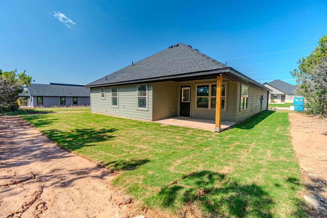 back of property featuring a lawn, a patio, and a shingled roof