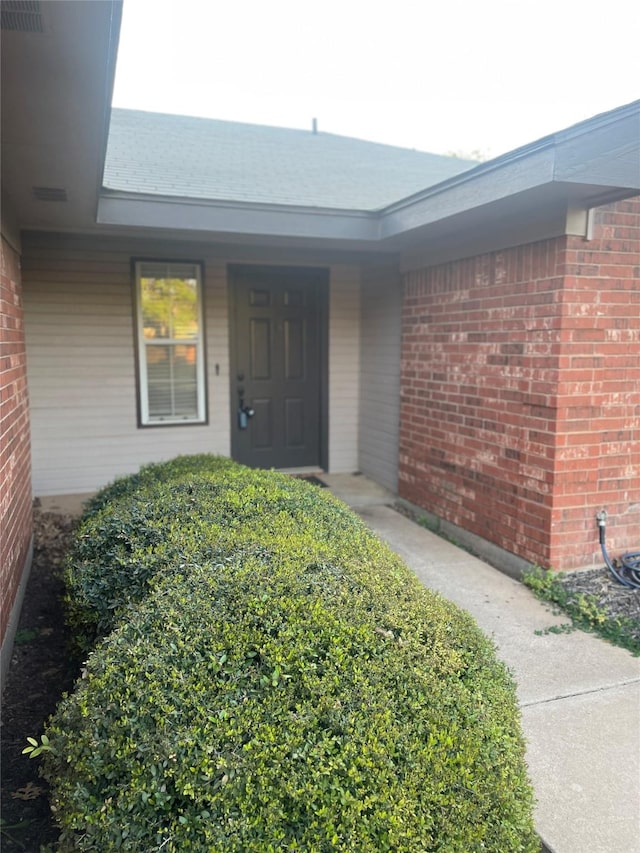 view of exterior entry with brick siding and visible vents