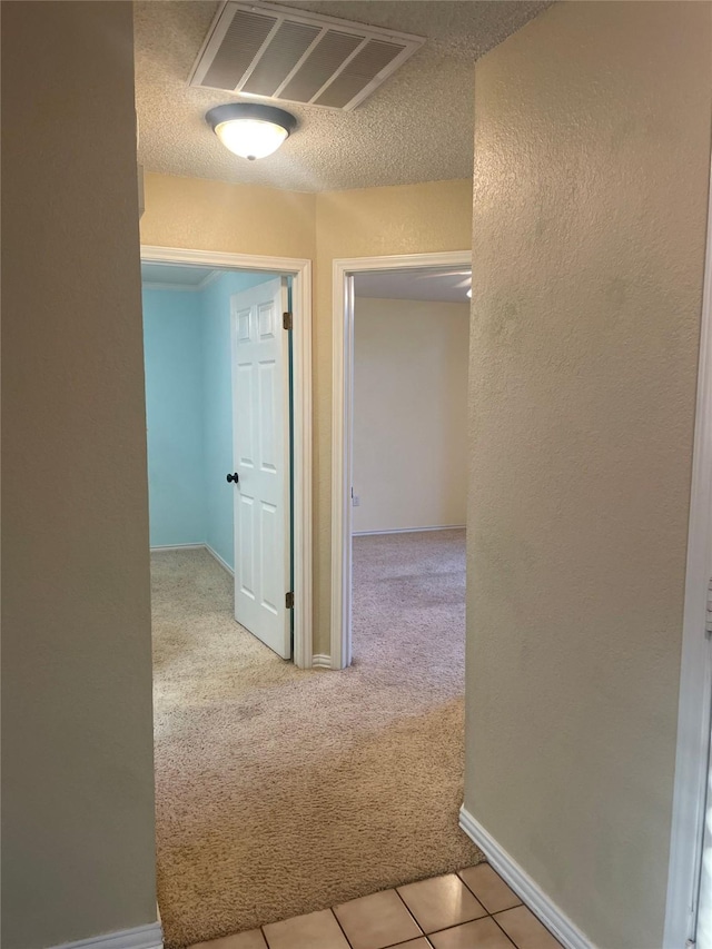 hallway featuring a textured ceiling, visible vents, baseboards, a textured wall, and carpet flooring