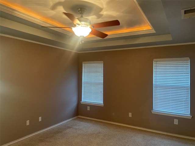 carpeted spare room with plenty of natural light, a raised ceiling, baseboards, and a ceiling fan