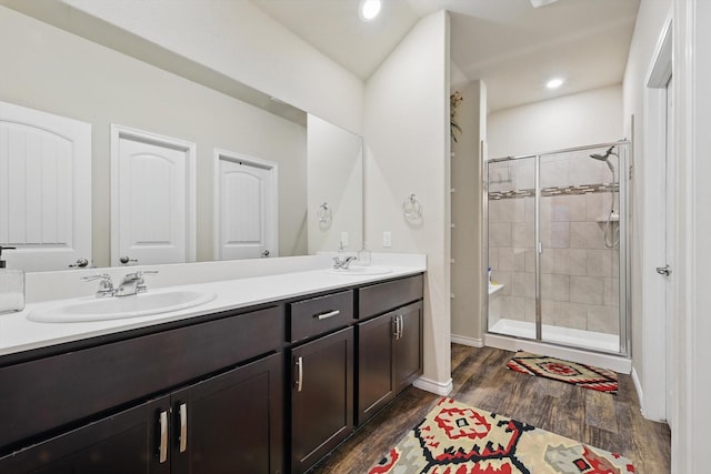 full bathroom with double vanity, a shower stall, a sink, and wood finished floors