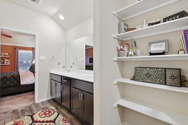 ensuite bathroom featuring a sink, double vanity, wood finished floors, lofted ceiling, and ensuite bathroom
