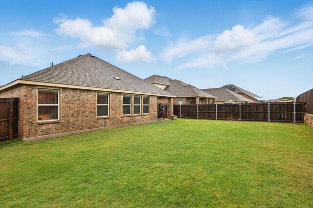 rear view of property featuring a fenced backyard, a shingled roof, a yard, and brick siding