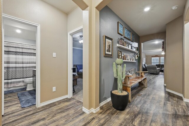 hall featuring arched walkways, baseboards, and wood finished floors