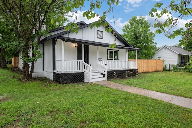 bungalow with covered porch, fence, and a front lawn