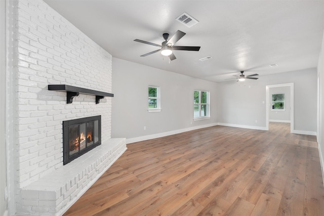 unfurnished living room with visible vents, a brick fireplace, light wood-style floors, baseboards, and a ceiling fan