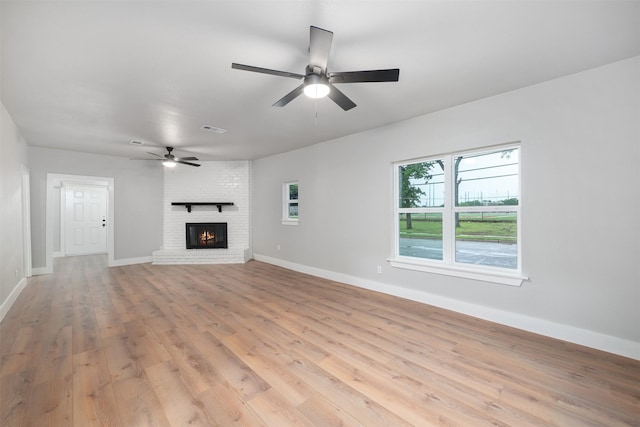 unfurnished living room featuring ceiling fan, visible vents, a brick fireplace, baseboards, and light wood-style flooring
