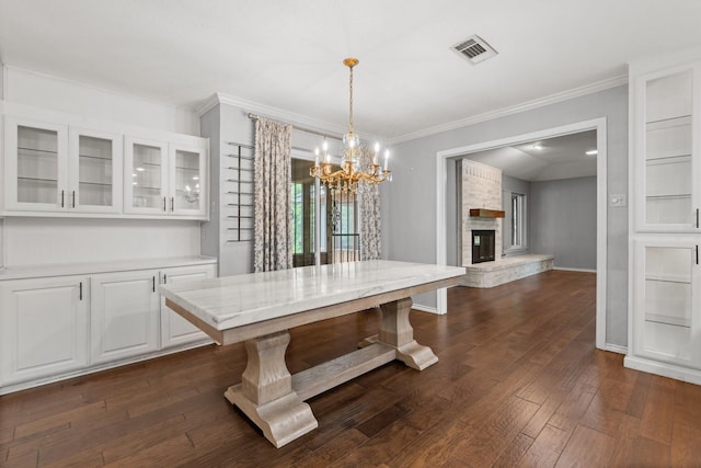 unfurnished dining area with visible vents, a fireplace, dark wood finished floors, a chandelier, and ornamental molding