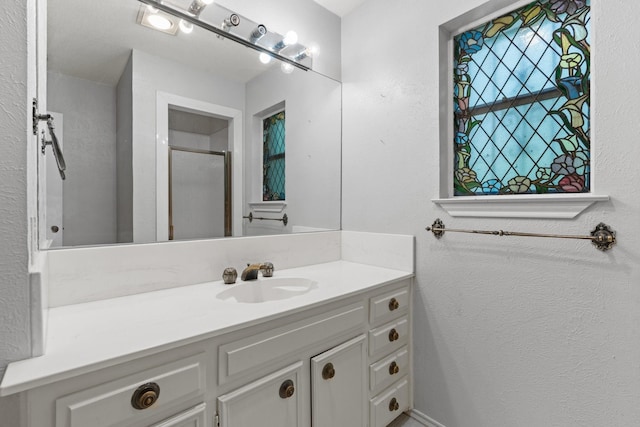 full bathroom featuring vanity, a textured wall, and a shower with shower door