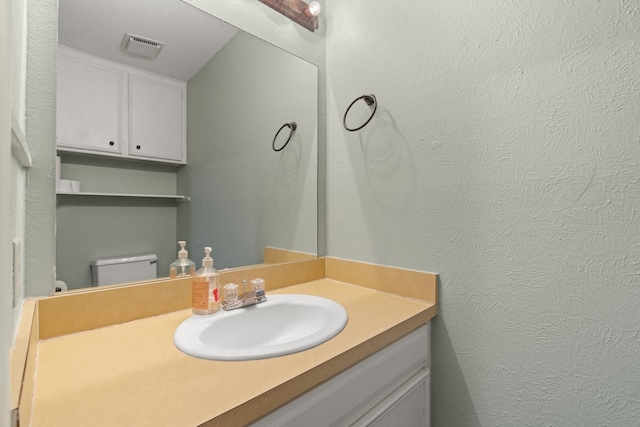 half bathroom with vanity, a textured wall, and visible vents