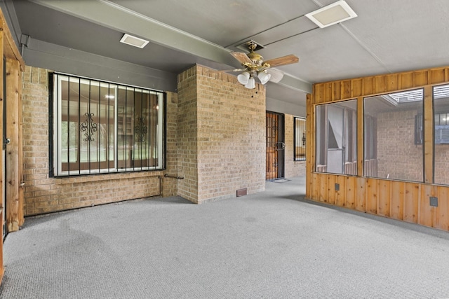 empty room with carpet, a ceiling fan, wood walls, and brick wall