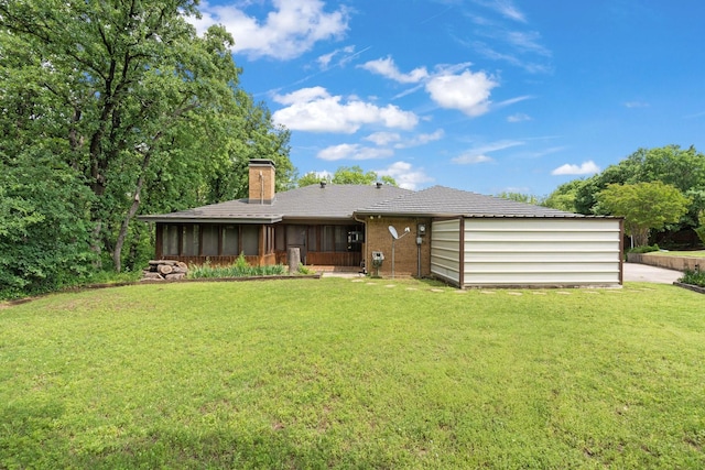 rear view of house featuring a lawn, brick siding, a chimney, and a sunroom