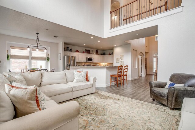 living area featuring visible vents, baseboards, a high ceiling, arched walkways, and light wood-style flooring