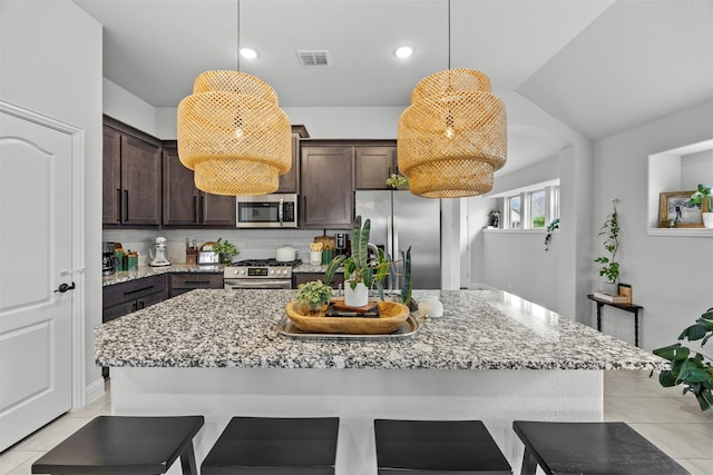 kitchen featuring dark brown cabinets, stainless steel appliances, a kitchen bar, and visible vents