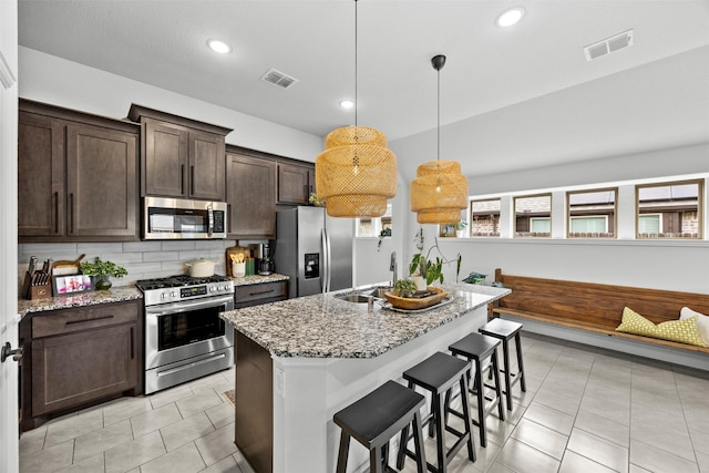 kitchen with visible vents, dark brown cabinets, light stone counters, a sink, and appliances with stainless steel finishes