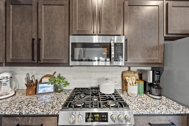 kitchen featuring backsplash, appliances with stainless steel finishes, dark brown cabinetry, and light stone counters