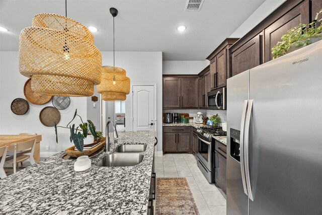 kitchen featuring dark brown cabinets, light stone countertops, appliances with stainless steel finishes, and a sink