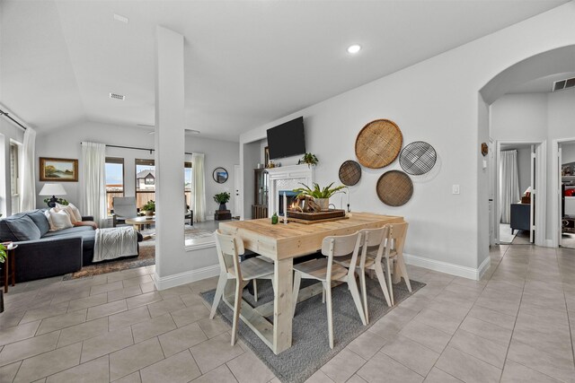 dining space featuring a lit fireplace, visible vents, arched walkways, vaulted ceiling, and light tile patterned floors